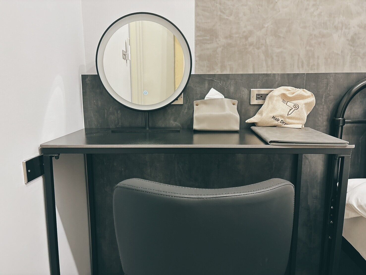 A bathroom vanity with a round mirror, a towel, and a hair dryer on a black countertop.