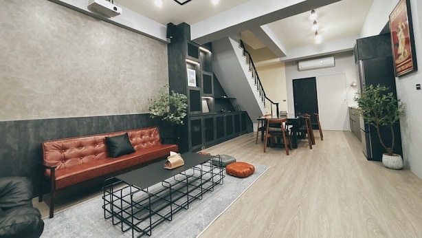 Un'ampia zona giorno con un divano rosso, un tavolino da caffè e un tavolo da pranzo con sedie. Si vede una scala che conduce a un altro piano.