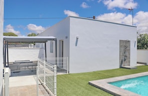 A modern white building with a swimming pool, a covered patio, and a fenced area.