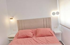 A bed with a headboard, two bedside tables, and wall-mounted lights.