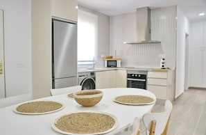 A modern kitchen with stainless steel appliances, a dining table with woven placemats, and a clean, minimalist design. - Chalet Ruperto III . (Conil de la Frontera)