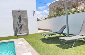 A swimming pool with a stone border, a covered outdoor seating area, and a grassy patio.