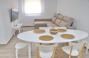 A modern living room with a round white table, four woven placemats, and a beige sofa.