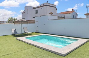 A rectangular swimming pool with a tiled edge, surrounded by a well-maintained lawn and two lounge chairs.