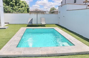 A rectangular swimming pool with tiled edges, surrounded by a grassy lawn and white walls.