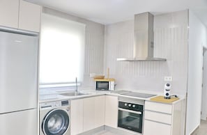 A modern kitchen with a washing machine, oven, microwave, and a built-in stove.