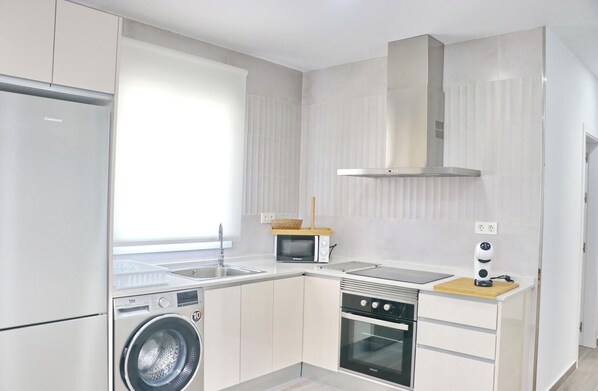 A modern kitchen with a washing machine, oven, microwave, and a built-in stove.