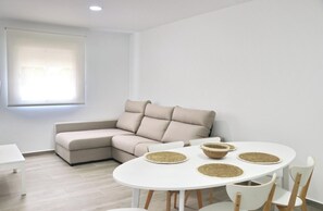 Un salon moderne avec un canapé d’angle beige, une table ronde blanche agrémentée de sets de table en fibres naturelles et une chaise blanche.
