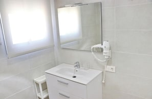 A bathroom with a white sink, a mirror, and a hairdryer on a wall-mounted stand.