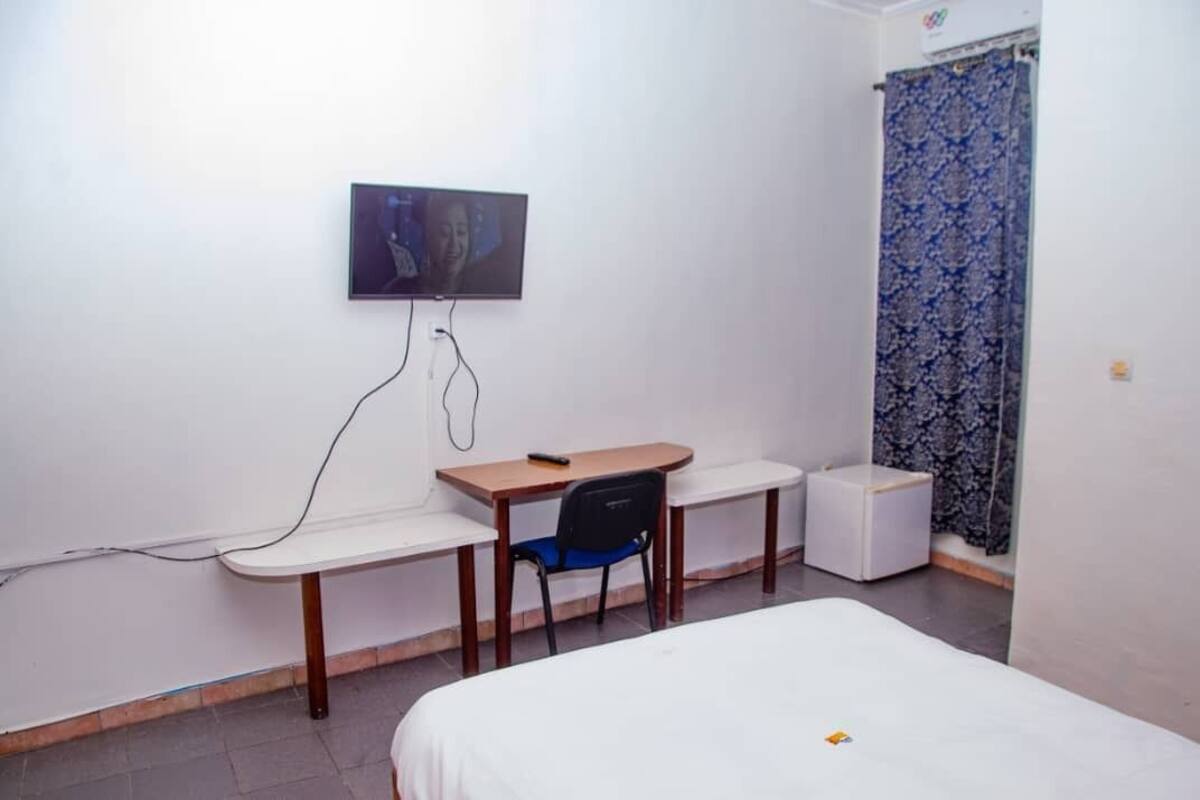 A small, clean room with a bed, a desk, a chair, and a television on the wall.