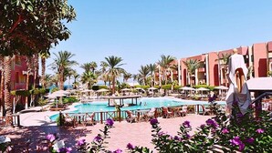 Poolbereich eines Resorts mit Palmen, Liegestühlen und einer Statue.