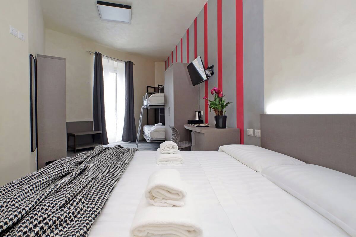 A hotel room with a large bed, a desk, a chair, a TV, and a potted plant.