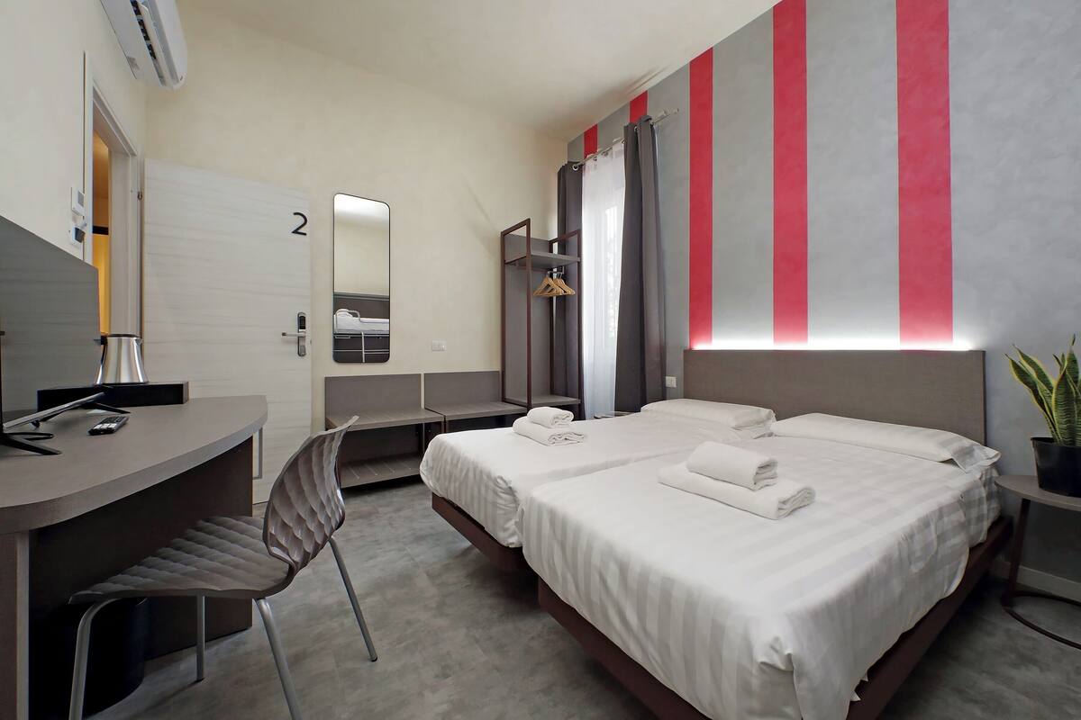 A modern hotel room with a bed, desk, chair, and a shower area.