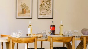 Zona pranzo con tavoli e sedie in legno, opere d'arte appese alla parete e bottiglie di vino e acqua sui tavoli.
