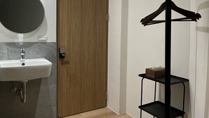 A modern bathroom with a wooden door, a round mirror, a sink, and a black metal shelf with a tissue box. - Wu Sheng Stay (Tainan)