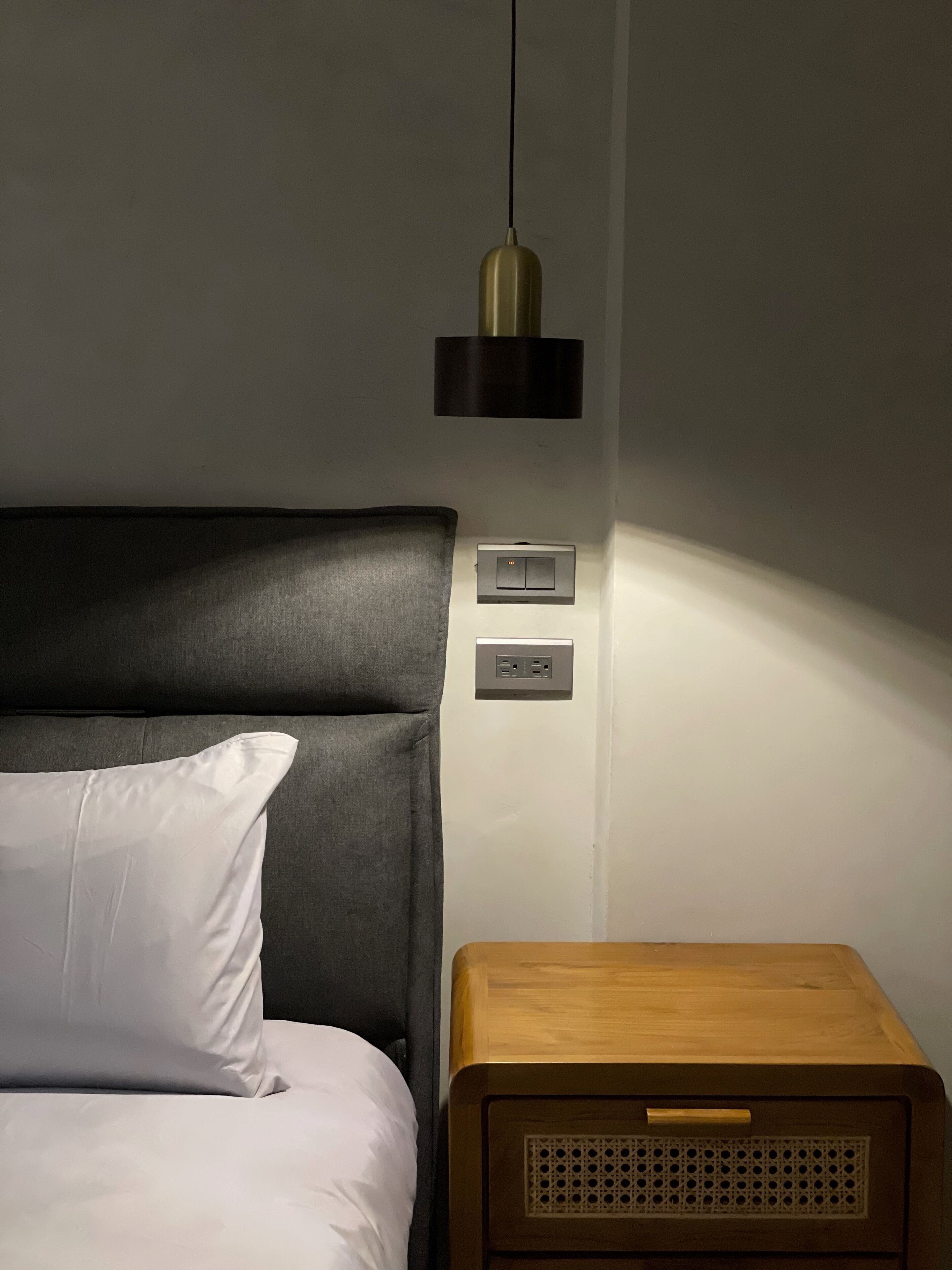 Un dormitorio con cama, mesita de noche, enchufe y lámpara colgante.