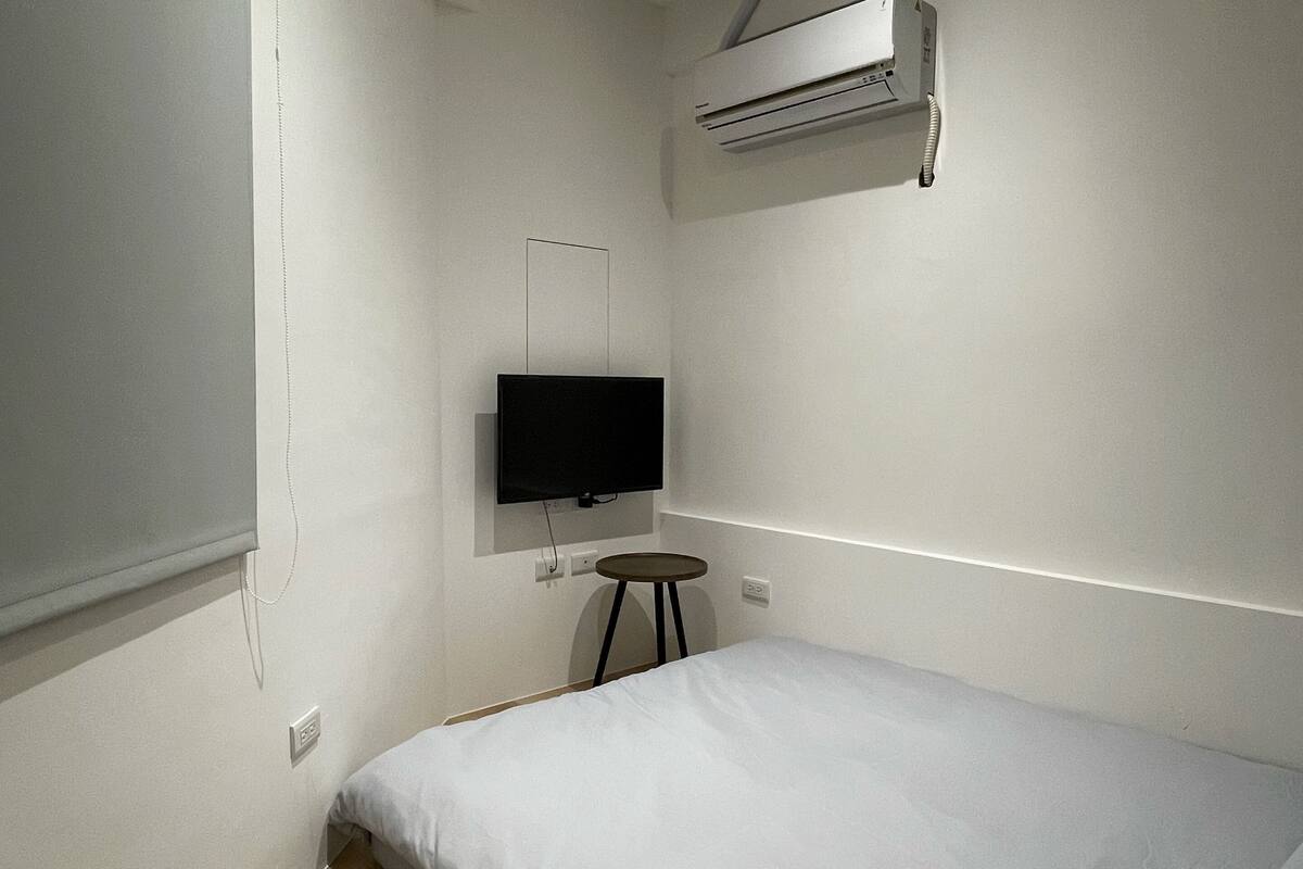 Quarto pequeno e moderno com uma cama de solteiro, TV fixada na parede e um aparelho de ar condicionado acima.
