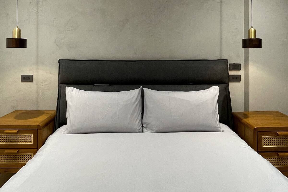 Quarto de hotel moderno com uma cama grande, duas mesas de cabeceira e luminárias pendentes.