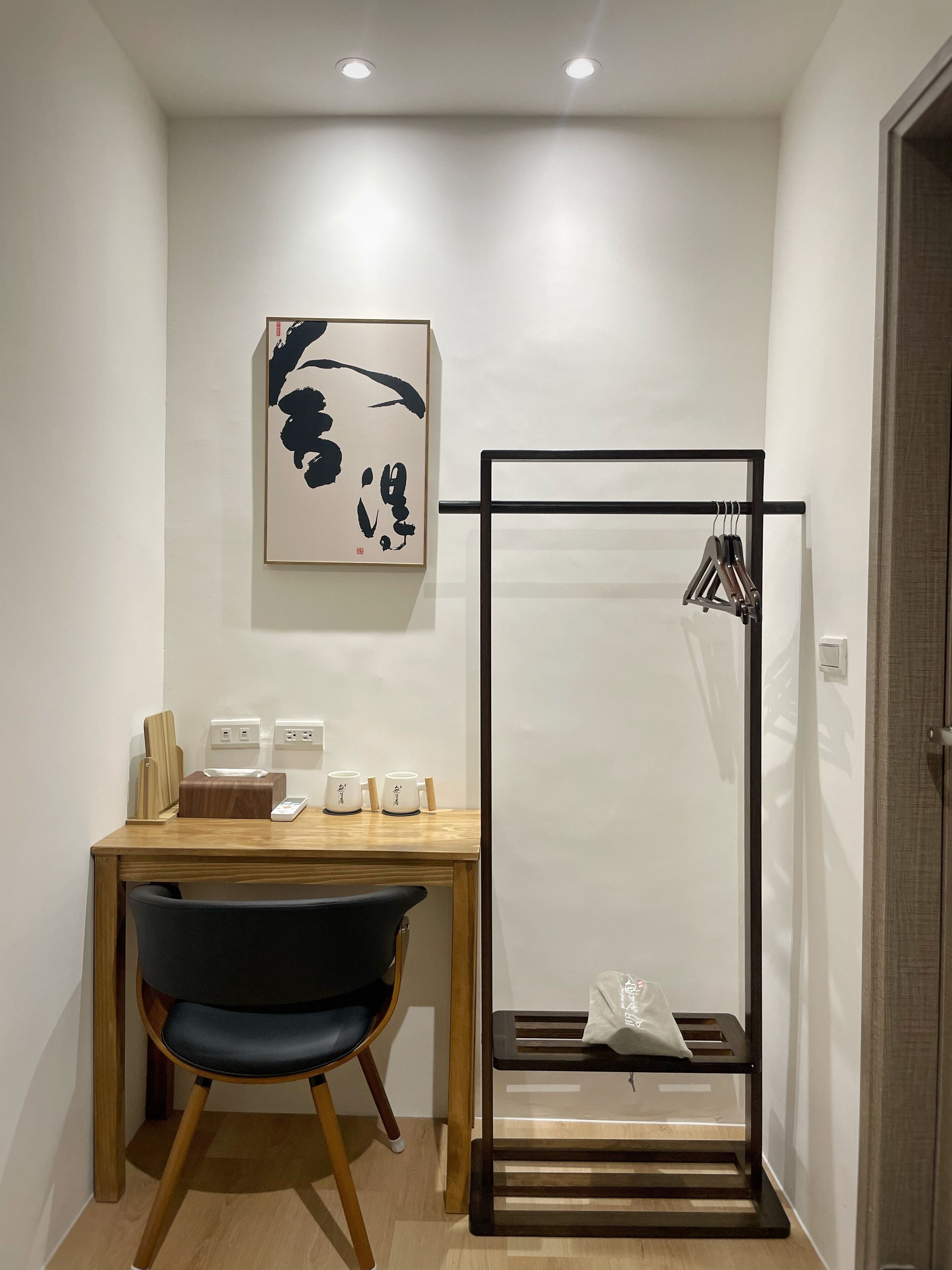 A modern room with a wooden desk, a black chair, a framed artwork, and a black metal rack with clothes.