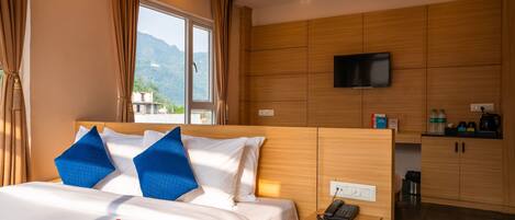 Quarto de hotel com uma cama, mesa de cabeceira com telefone, televisão na parede e vista para montanhas pela janela.