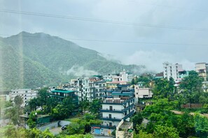 A densely built hillside town with multi-story buildings, surrounded by lush greenery and mountains.