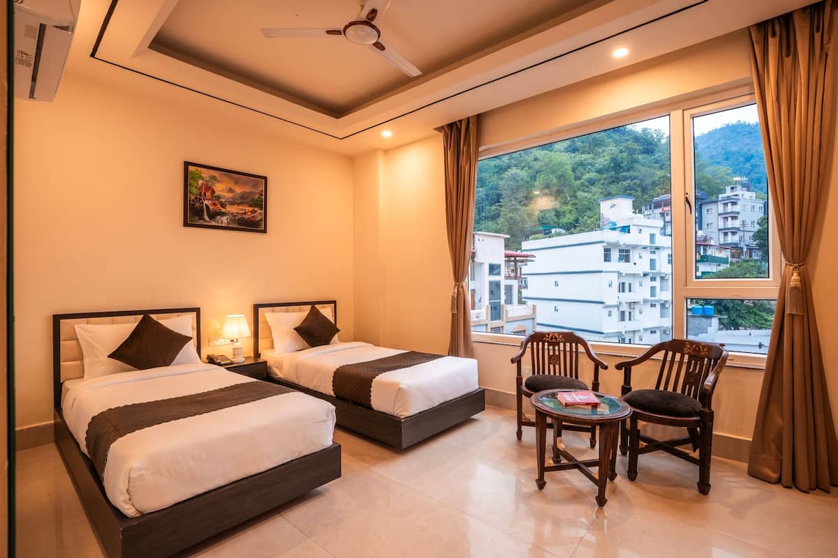 Habitación de hotel con dos camas, una mesita con sillas, un cuadro en la pared y vistas a edificios por la ventana.