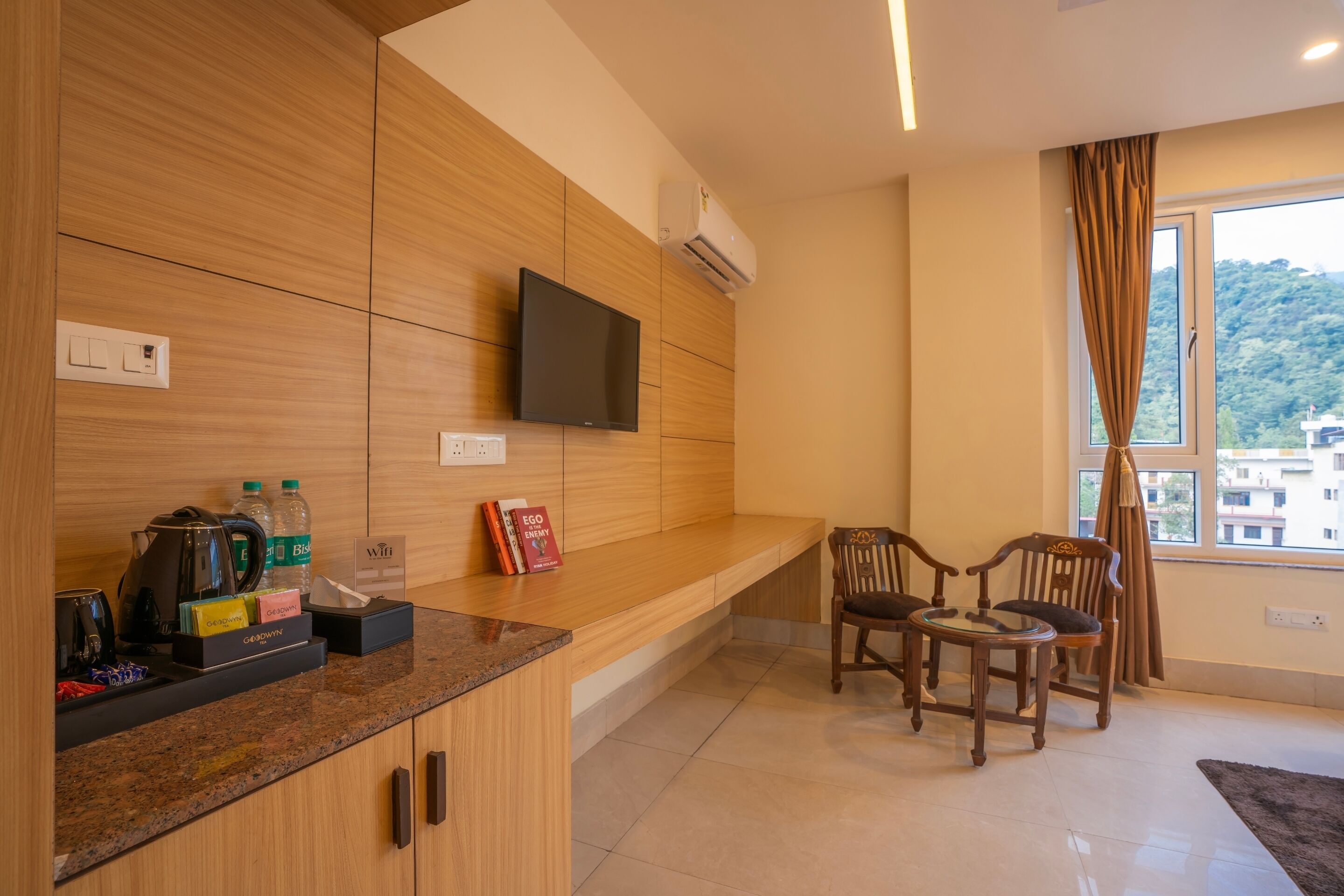 Una habitación moderna con paneles de madera, un televisor de pantalla plana, una zona de café y un rincón de descanso con dos sillones.
