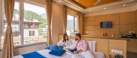 A hotel room with a bed, a TV, a bedside table, and a view of a mountain.