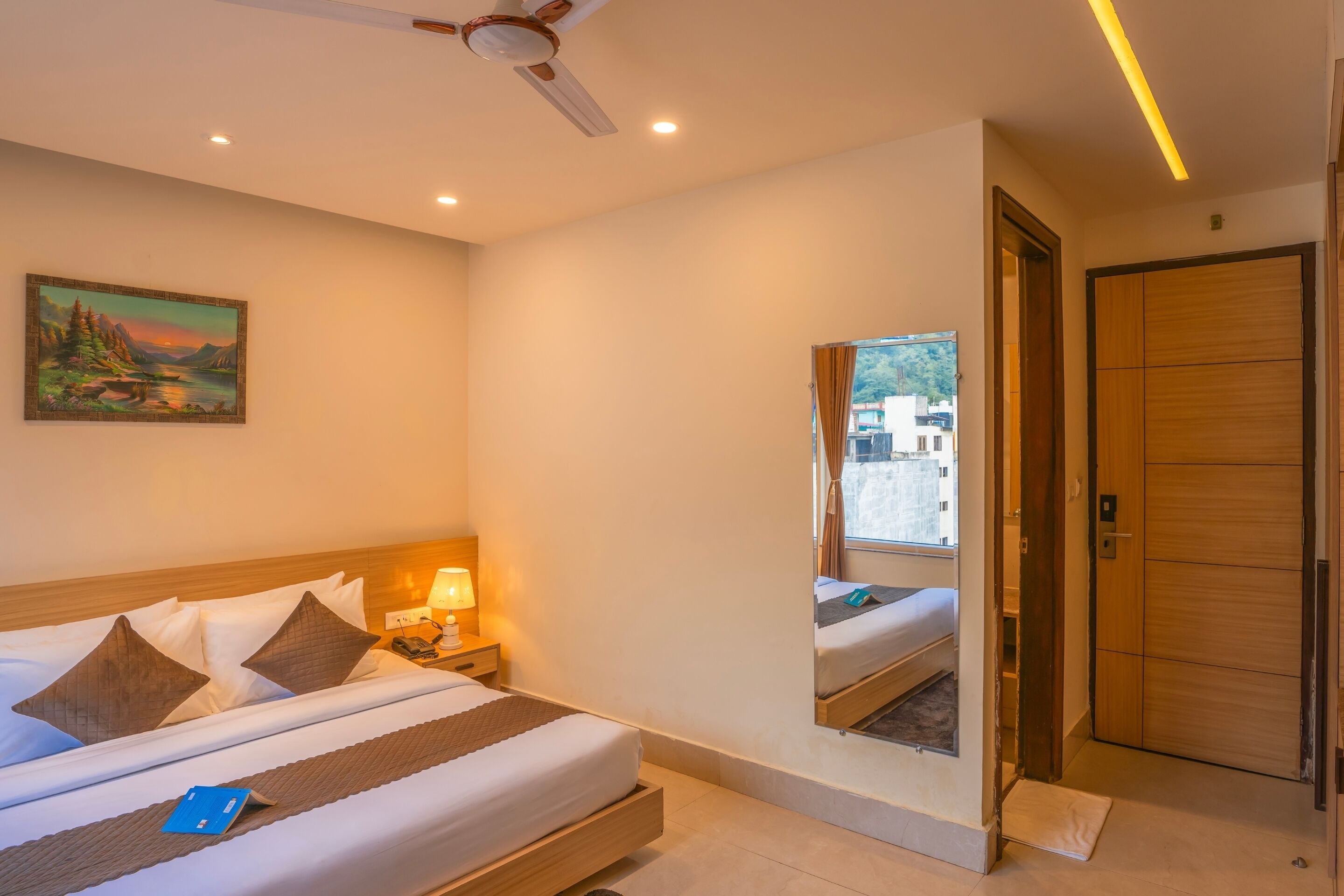 Habitación de hotel con cama, mesita de noche, lámpara y un espejo grande que refleja la habitación.