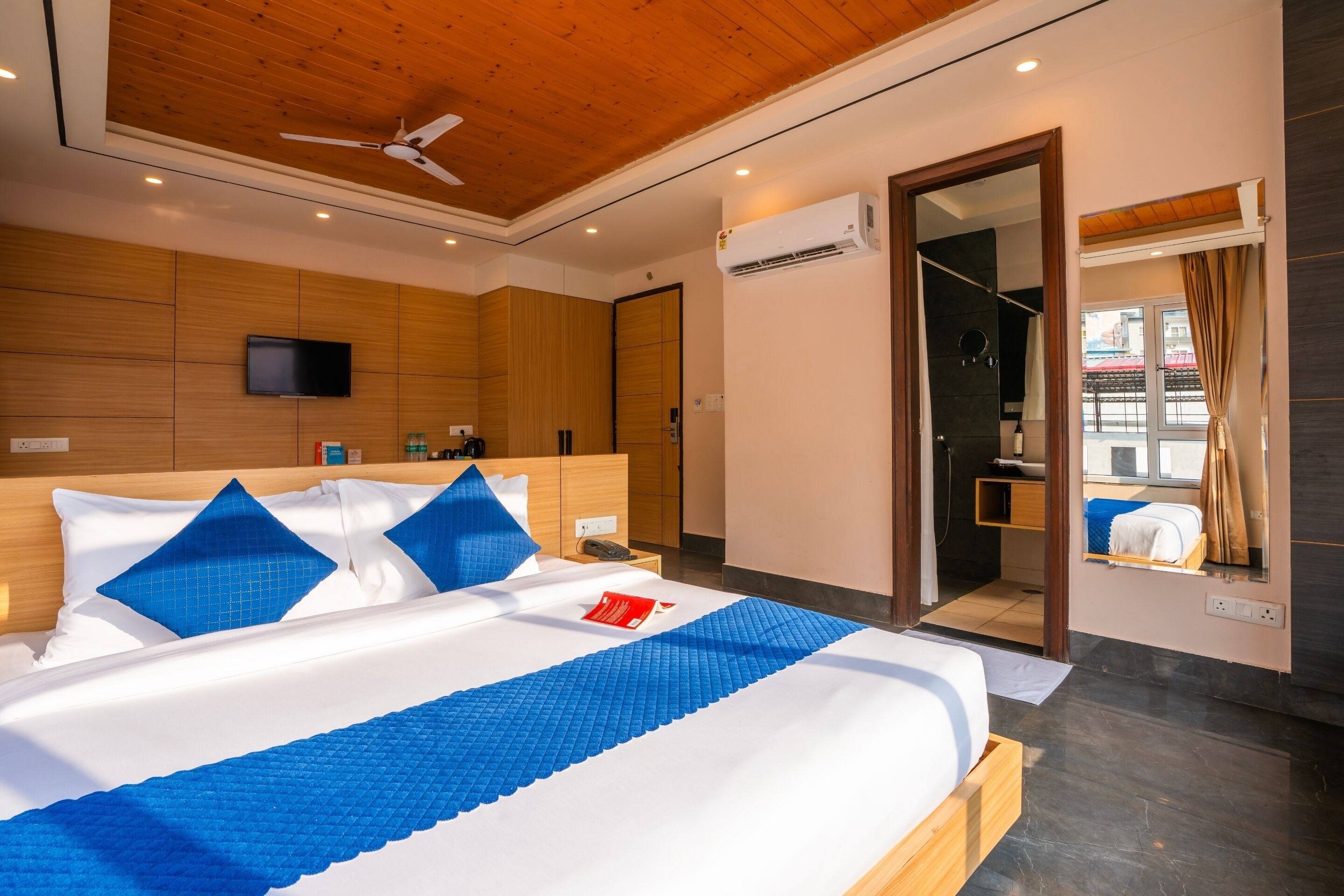 Een moderne hotelkamer met een houten plafond, een groot bed met blauw beddengoed, een flatscreen televisie en een airconditioning.