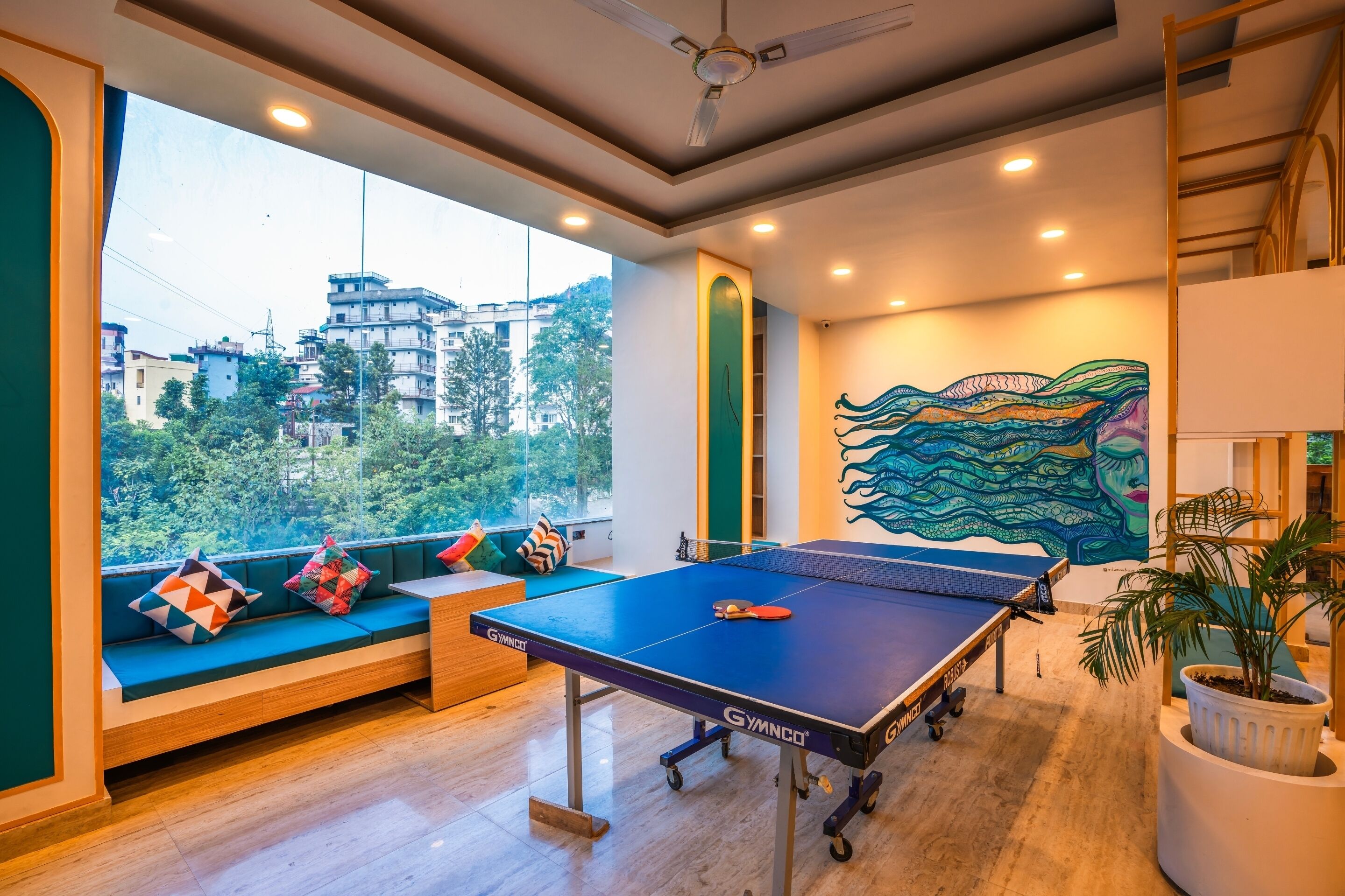 A ping pong table in a modern room with a view of buildings and trees.