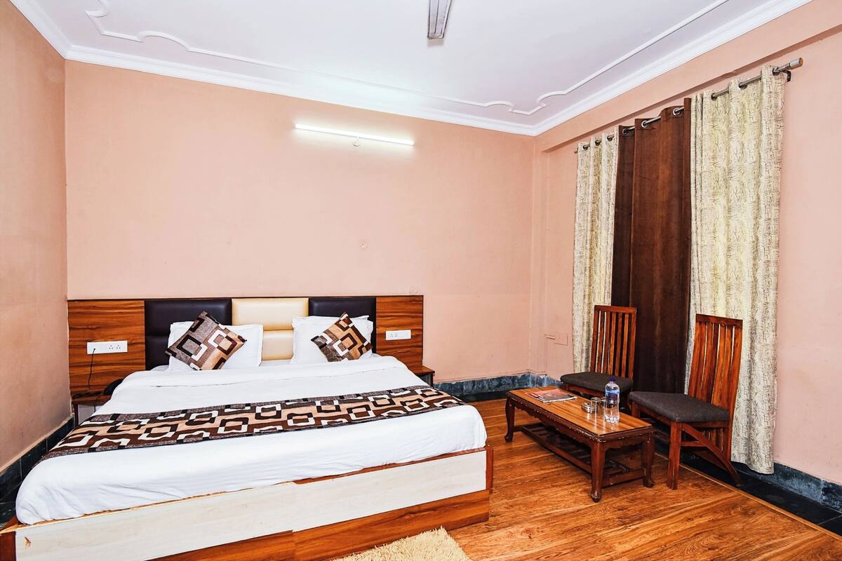 Une chambre d’hôtel avec un grand lit, une table de chevet en bois, une petite table avec des chaises et une fenêtre avec des rideaux.