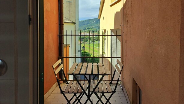 A narrow balcony with a wooden table and two chairs, overlooking a scenic view of green fields and hills. - Appartamento Trigoso (Sestri Levante)