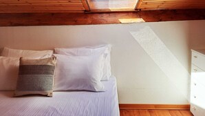 A bedroom with a skylight, wooden ceiling, a bed with white and patterned pillows, and a white dresser. - Appartamento Trigoso (Sestri Levante)