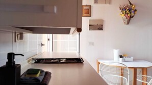A modern kitchen with a gas stove, a sink, and a window. There is a dining area with a white table and chairs. - Appartamento Trigoso (Sestri Levante)