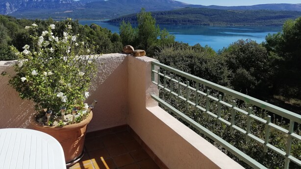 A balcony with a potted plant, a white table, and a view of a lake and mountains. - 3-room apartment 55 m2, terrace 15 m2, breathtaking view, sleeps 4, air-conditioned, WIFI (Sainte-Croix-du-Verdon)