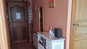 A hallway with a wooden door, a white cabinet with books, a thermostat, and a small painting on the wall. - 3-room apartment 55 m2, terrace 15 m2, breathtaking view, sleeps 4, air-conditioned, WIFI (Sainte-Croix-du-Verdon)