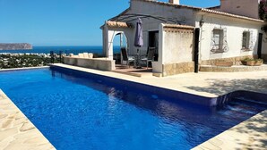 A poolside area with a clear view of the sea, a small building with a tiled roof, and a patio with outdoor seating. - Villa- Lagarto in Panorama (Javea)