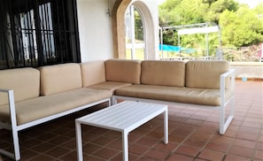 Relax in this outdoor seating area with a comfortable sofa and table, surrounded by a large window and terracotta tiles.