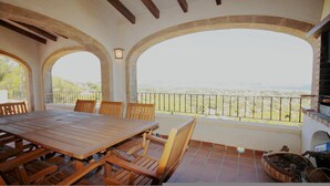 An outdoor patio with a wooden table and chairs, stone arches, and a view of a distant landscape. - Villa- Lagarto in Panorama (Javea)