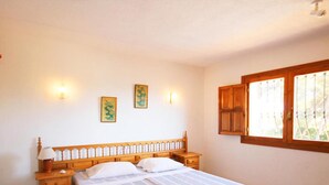 A bedroom with a wooden bed frame, two bedside tables, a nightstand, and a window with wooden shutters. - Villas Perret in Panorama (Javea)