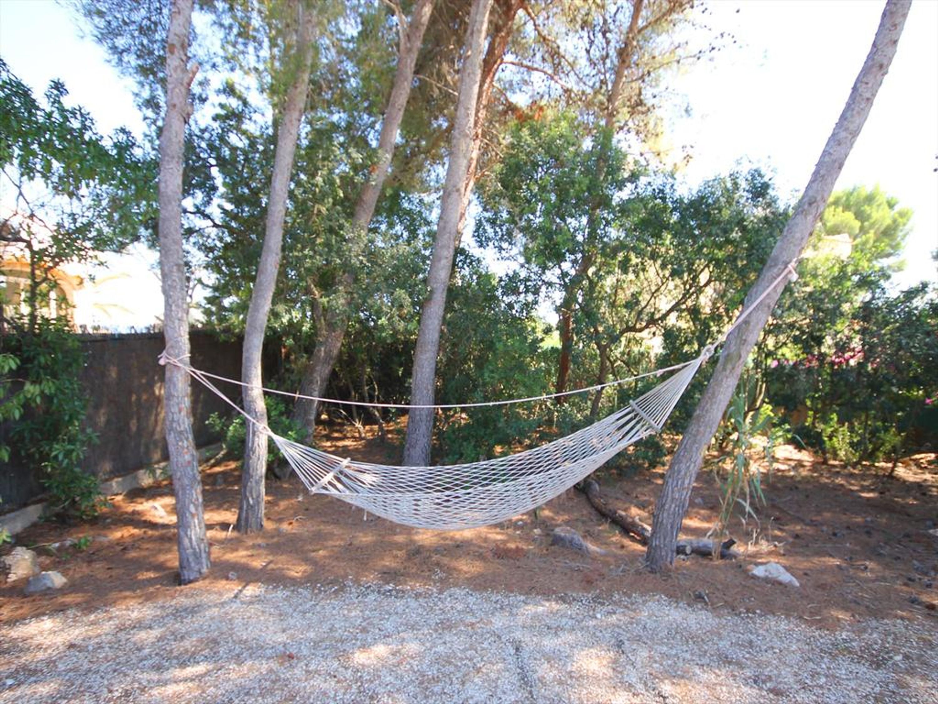 A hammock tied between trees in a wooded area with gravel ground.