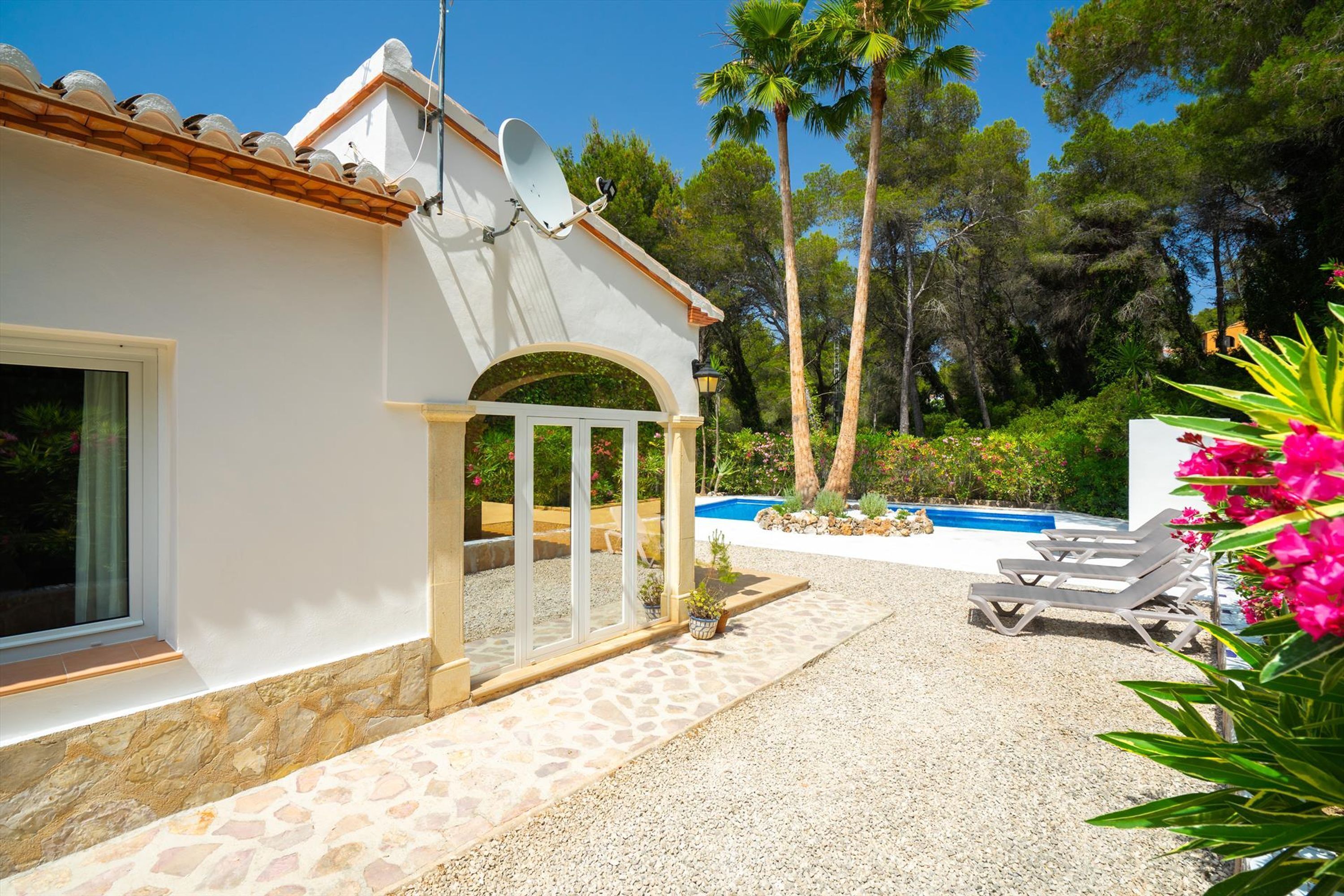 A white building with a stone patio, a pool, and lounge chairs.