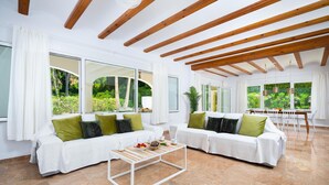 A spacious living room with a white sofa set, a coffee table, and large windows offering a view of greenery. - Villa Alma in El Tosalet (Javea)