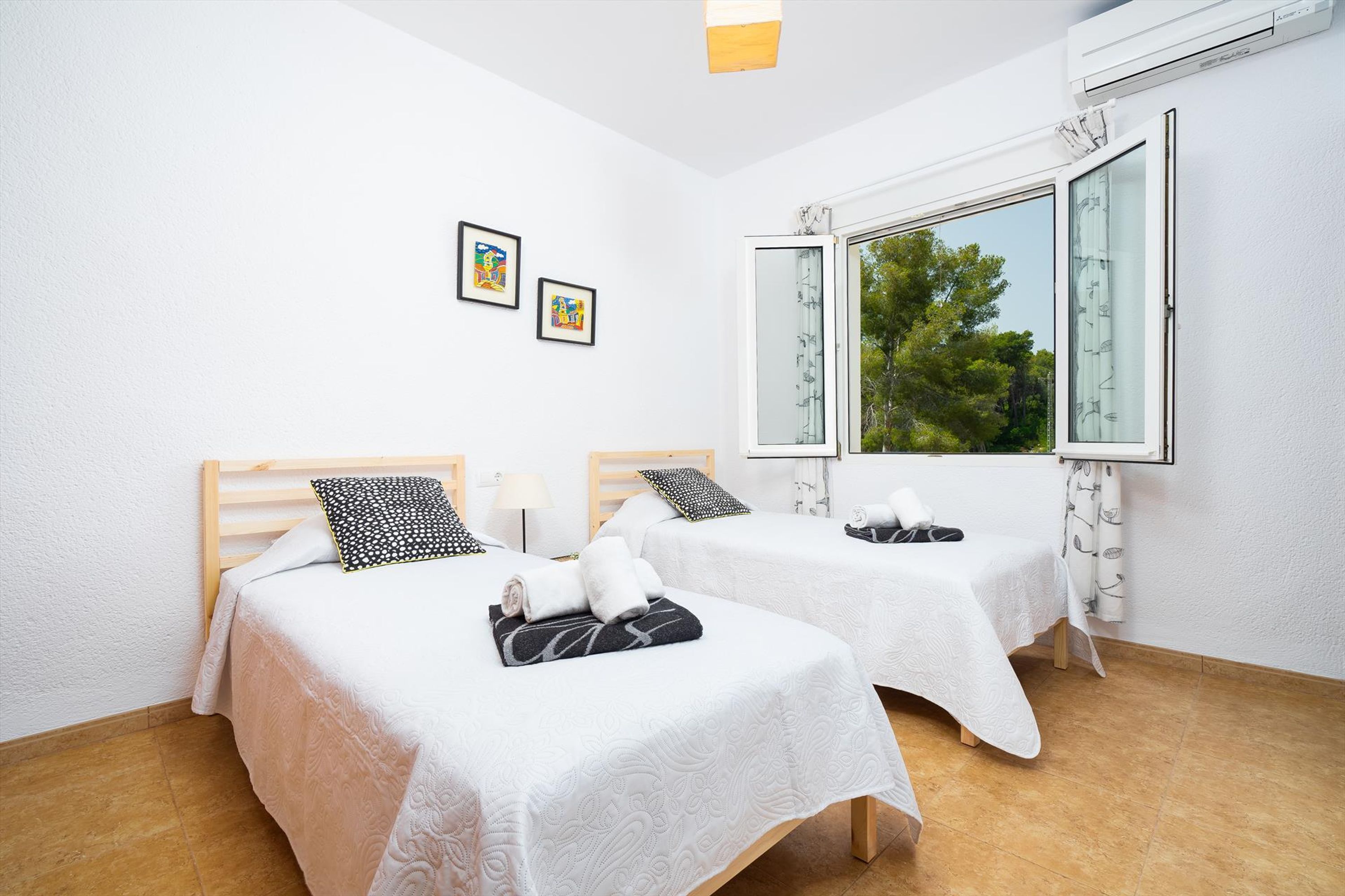 A room with two beds, white walls, and a window with a view of trees.