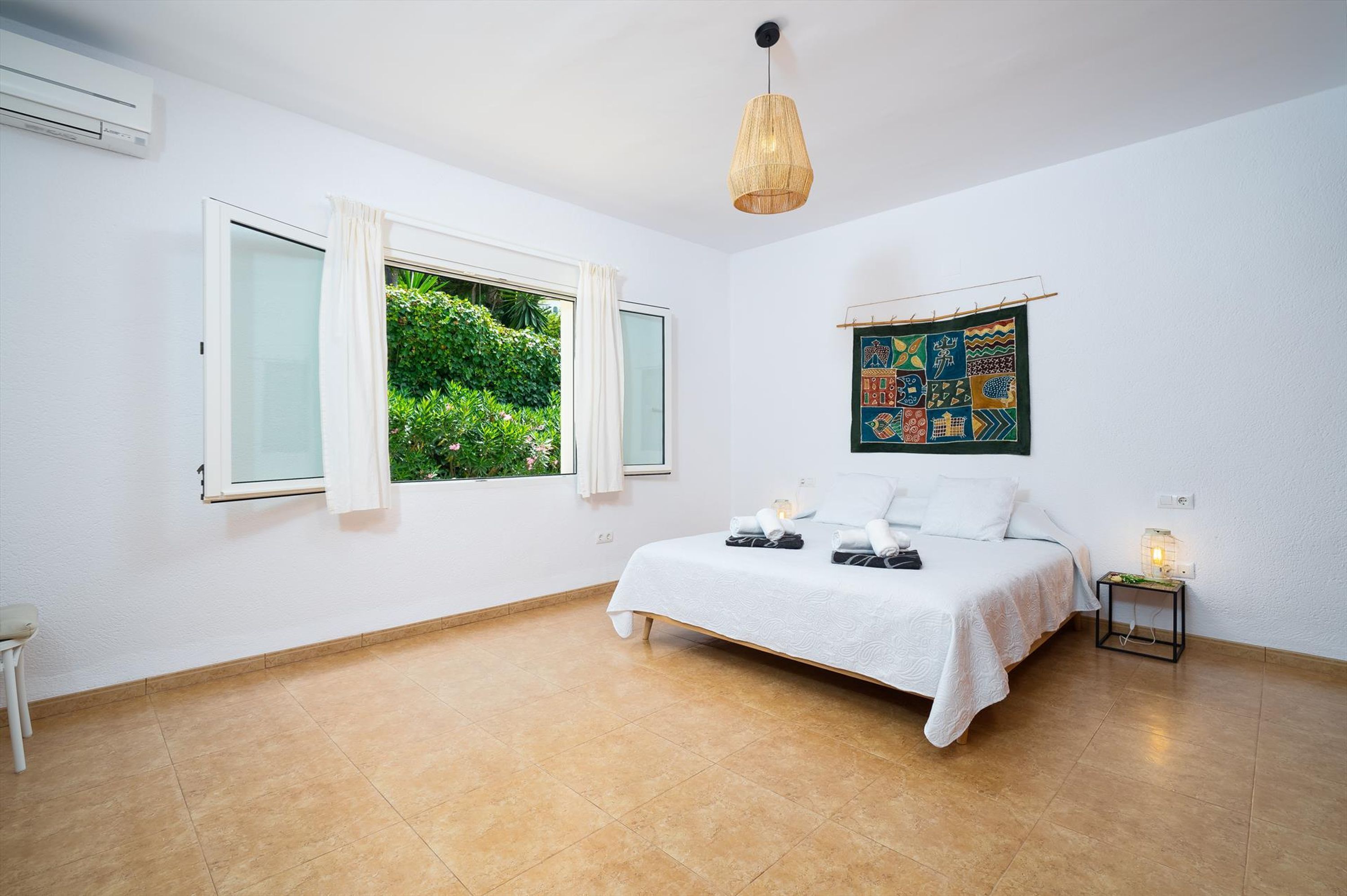 Un dormitorio con cama, ventana con cortinas, una obra de arte en la pared y una mesita de noche con lámpara.