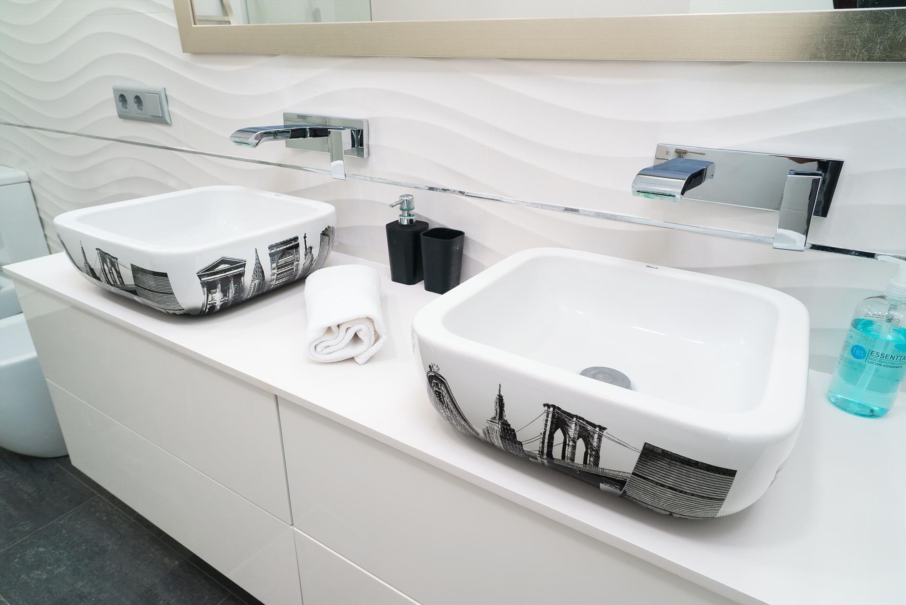 Een moderne badkamer met twee witte wastafels, een glazen plank en een spiegel.