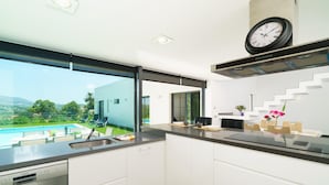 A modern kitchen with a built-in dishwasher, a large window overlooking a swimming pool and greenery, and a clock on the wall. - Villa Vera in Javea With 4 Bedrooms and 2 Bathrooms (Javea)