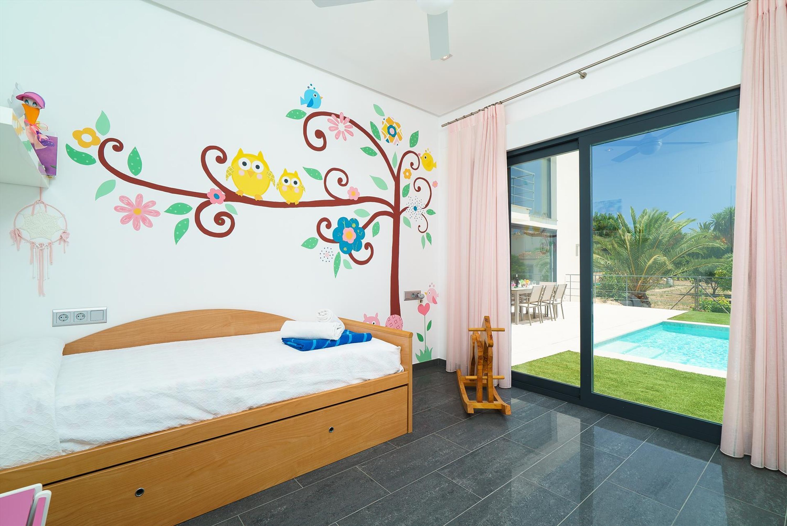 Un dormitorio con una cama, una mesita de noche de madera, un ventanal y vistas a una piscina.