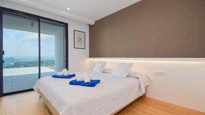 A modern hotel room with a large bed, a sliding glass door leading to a balcony, and a city view. - Villa Madi in Cumbre del Sol (Benitachell)